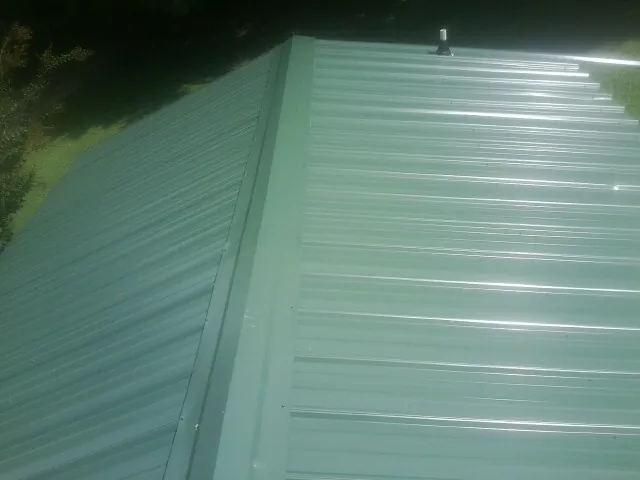 New green metal panels meeting at the ridge of a roof — Flat Roof Repair work by our crew in Raymond
